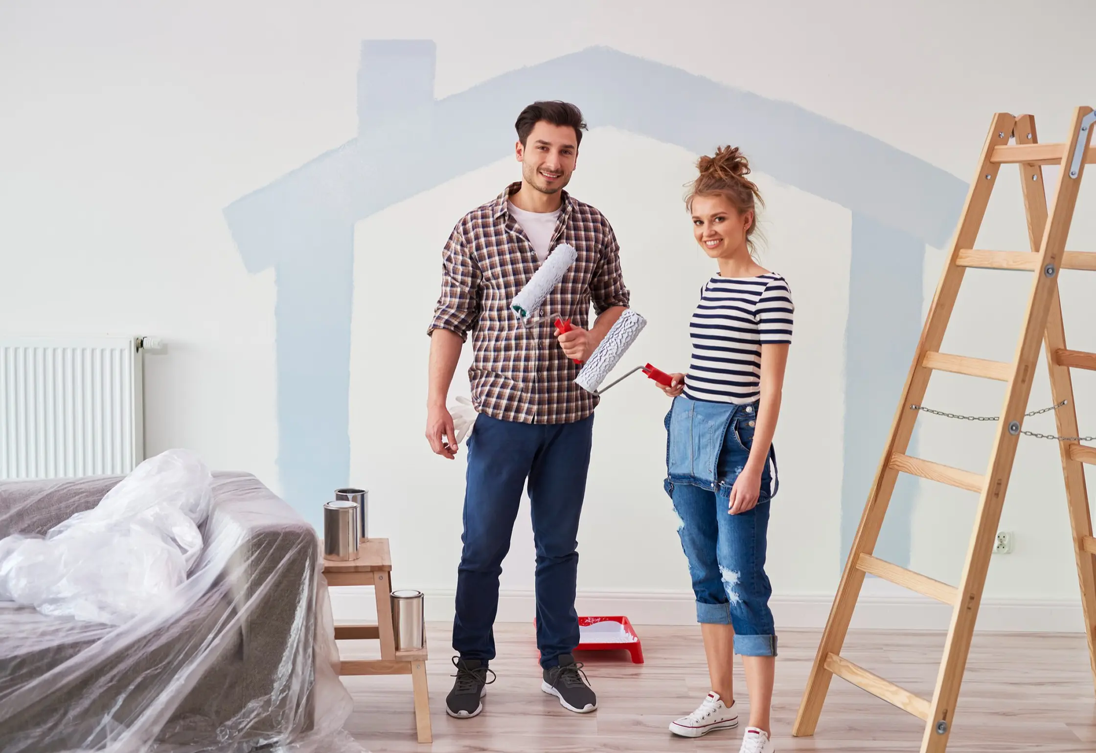 Two homeowners with paint rollers preparing a room for renovation